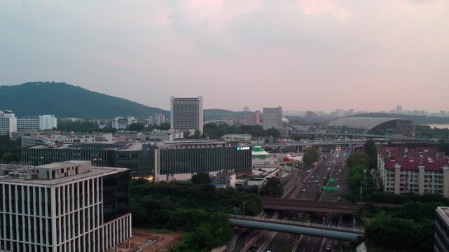 A panoramic urban view featuring buildings, a road, and a distant mountain under a soft dusk sky.