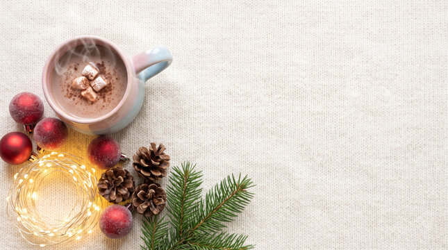 Warm cocoa flat lay with marshmallows, ornaments, and pinecones on knit copy space