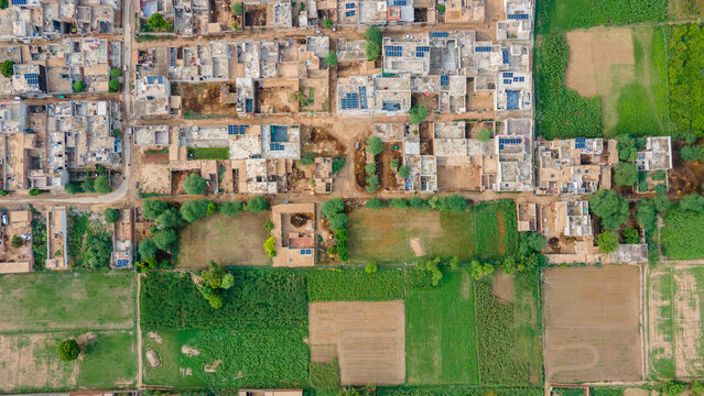 Aerial view of a rural village with traditional houses, flat rooftops, solar panels, and surrounding agricultural fields in Punjab, Pakistan.