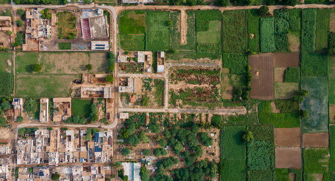 Aerial view of a rural village featuring traditional houses, dirt roads, and surrounding agricultural fields with green crops and patches of bare earth in Punjab, Pakistan.