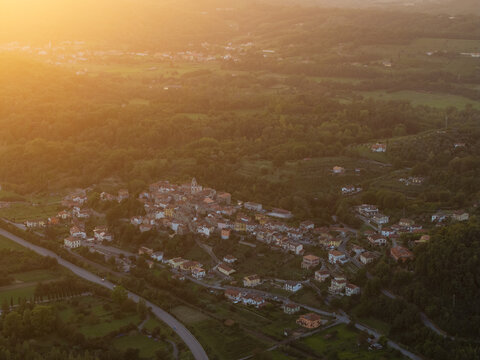 Aerial view of the village of Gassano nestled in the rolling hills of Tuscany during golden hour, featuring stone houses, lush greenery, and winding roads in Gassano, Tuscany, Italy.