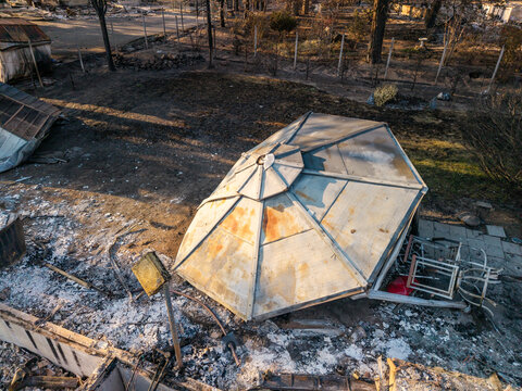 Aerial view of the aftermath of the Spokane wildfire, showing a collapsed patio umbrella amidst scorched earth and charred debris in Spokane, Washington, United States.