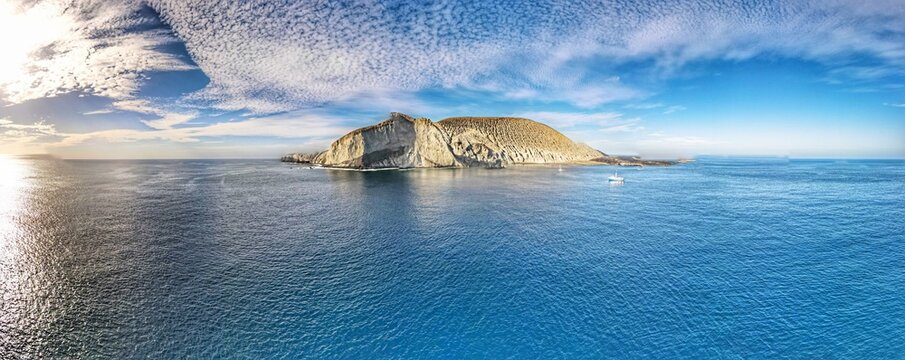 Aerial view of San Benedicto Island featuring rugged volcanic cliffs surrounded by the deep blue Pacific Ocean with a small boat nearby in Colima, Mexico.