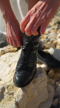 Boots leather hiking person tying their black leather combat boots while standing on white rocks on a sunny day