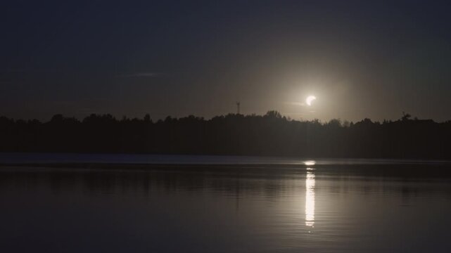 Solar eclipse over lake in timelapse at dusk