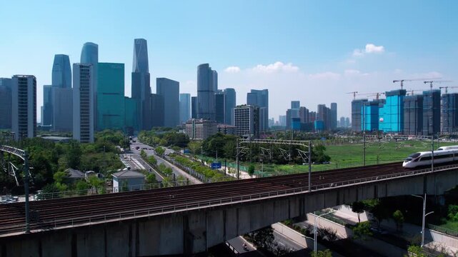 A modern high-speed train travels on an elevated viaduct against a backdrop of urban skyscrapers and construction sites.