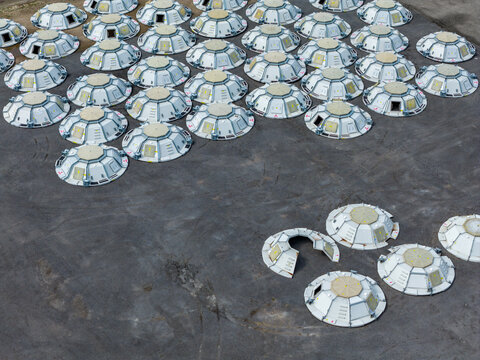 Aerial view of numerous prefabricated stainless steel storage tank roofs arranged in rows on a paved industrial site in North Holland, Netherlands.