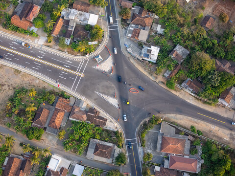 Aerial view of a road intersection surrounded by residential houses with tiled roofs and lush greenery in Bantul, Special Region of Yogyakarta, Indonesia.