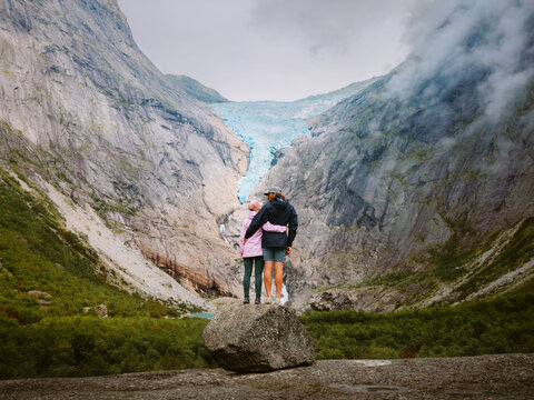 Couple travel in Norway embracing in mountains romantic vacations tour, family relationship bonding man and woman friends hiking sightseeing Briksdalsbreen glacier view adventure lifestyle outdoor