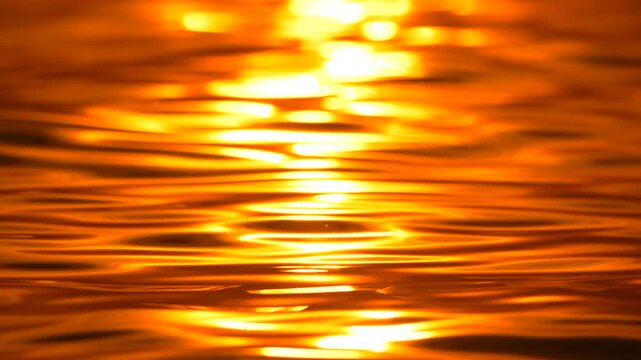 Golden water ripples mirror a bright sunlit horizon during evening, providing a serene outdoor background. Extreme close up locked off static shot.