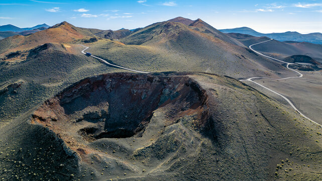 Aerial view of a volcanic crater in Timanfaya National Park with winding roads through the barren volcanic landscape in Lanzarote, Canarias, Spain.