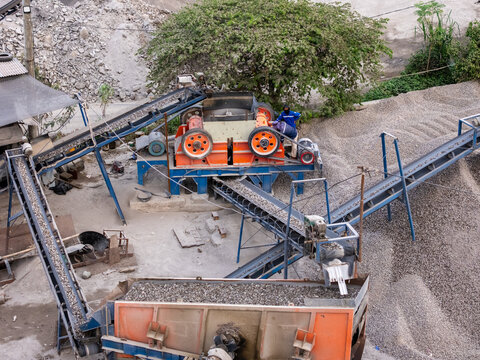 Aerial view of a stone crushing plant with conveyor belts transporting gravel, piles of crushed stone, and workers operating the machinery in Klaten, Central Java, Indonesia.