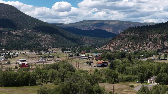 Summer aerial of rural mountain town South Fork Colorado with forested valleys with open fields featuring residential buildings in the La Garita Mountains