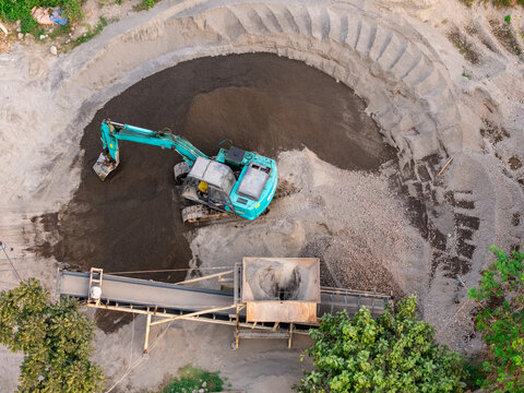 Aerial view of an excavator working in a sand and gravel quarry with a conveyor belt system in Manisrenggo, Central Java, Indonesia.