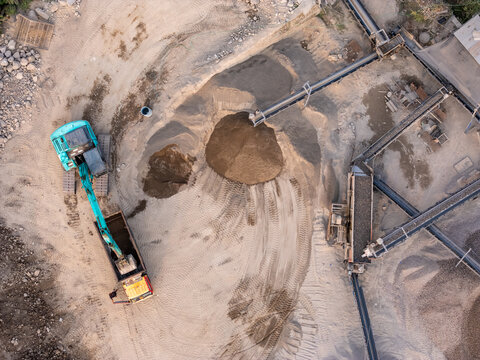 Aerial view of an excavator loading sand into a truck at a quarry site with conveyor belts and piles of aggregate in Manisrenggo, Central Java, Indonesia.