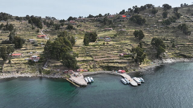 Aerial view of Taquile Island with its characteristic agricultural terraces, small houses, and a boat pier on the shore of Lake Titicaca in Huillanopampa, Puno, Peru.