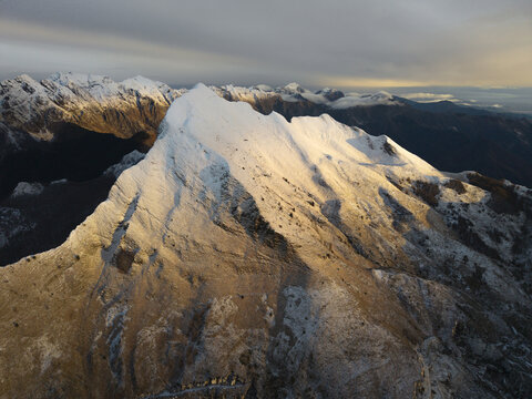 Aerial view of the snow-capped peaks of the Apuan Alps illuminated by golden hour light in Tuscany, Italy.