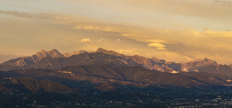 Aerial view of the Apuan Alps mountain range at sunset with rugged peaks and warm golden light over the landscape in Tuscany, Italy.