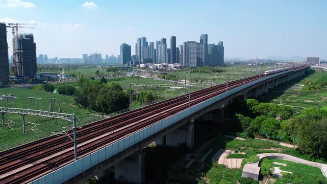 A high-speed train runs on an elevated railway bridge, with urban buildings and construction sites in the background.