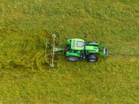 Aerial view of a green tractor pulling a hay rake across a lush green field in Valldal, More og Romsdal, Norway.