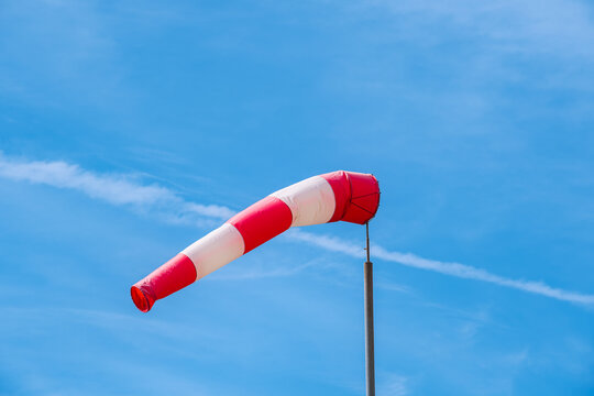 A red-and-white weather vane blowing in the wind against a blue sky