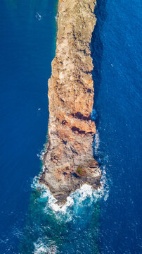 Aerial view of Socorro Island featuring rugged volcanic rock formations and steep cliffs surrounded by deep blue ocean waters with white surf crashing against the coastline in Colima, Mexico.