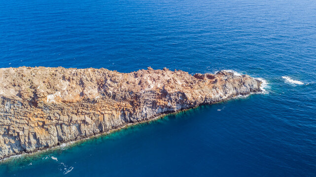 Aerial view of Socorro Island with rugged volcanic cliffs and rocky terrain meeting the deep blue Pacific Ocean in Colima, Mexico.