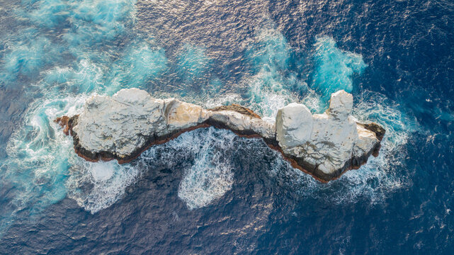 Aerial view of Roca Partida rock formation surrounded by deep blue ocean water with white waves crashing against the rugged cliffs in Mexico.