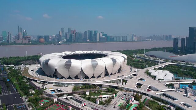 A large lotus-shaped modern stadium stands by a wide river, with urban skyline in the background on a clear day.