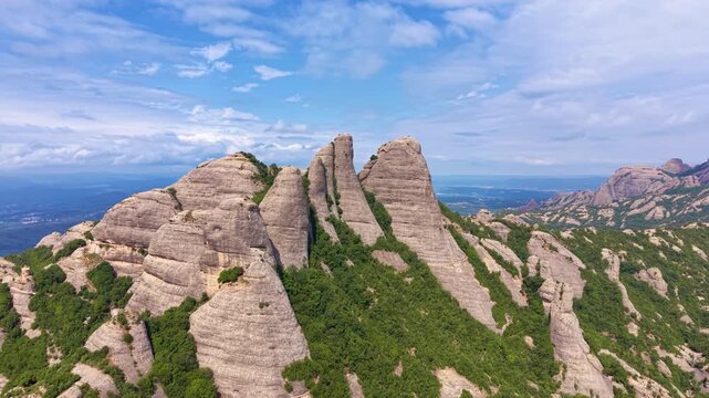 Panoramic view of the iconic serrated conglomerate rock formations of Montserrat mountain massif in Catalonia, Spain, with lush green vegetation and blue sky