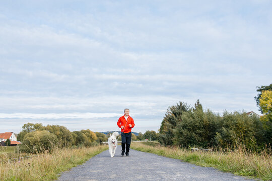 Man exercising with his samoyed dog on a path, staying active and healthy.