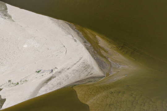 Aerial view of sandbanks and low water levels in a river, showing exposed sediment and murky water patterns in Poland.