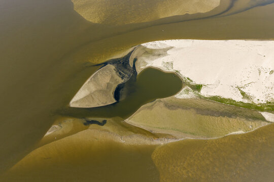 Aerial view of exposed sandbanks and low water levels in a river, showing sediment patterns and shallow water channels in Poland.