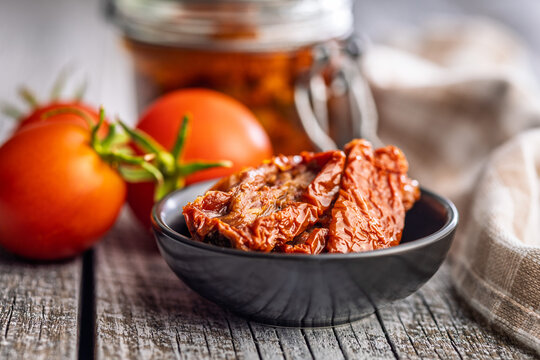 Close-Up Of Sun-Dried Tomatoes In Bowl With Fresh Tomatoes On Rustic Wooden Table