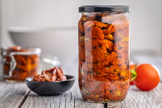 Jar of Sun-Dried Tomatoes in Oil on Rustic Wooden Table With Bowl and Fresh Tomatoes