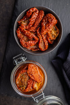 Sun-Dried Tomatoes in Olive Oil Jar and Bowl on Dark Slate for Gourmet Mediterranean Cooking