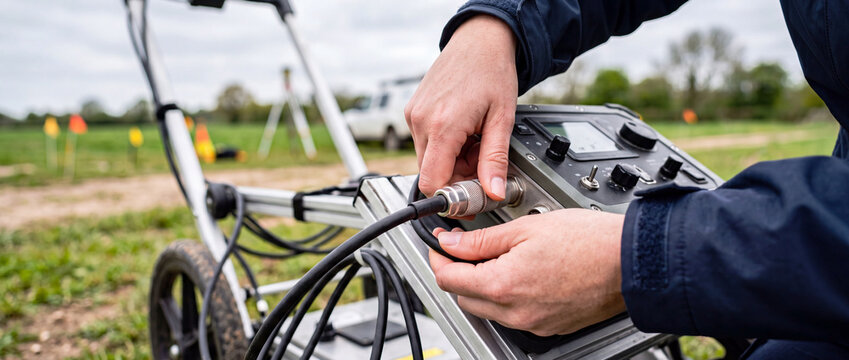 Technician setting up ground penetrating radar utility locator on wheeled cart for field survey