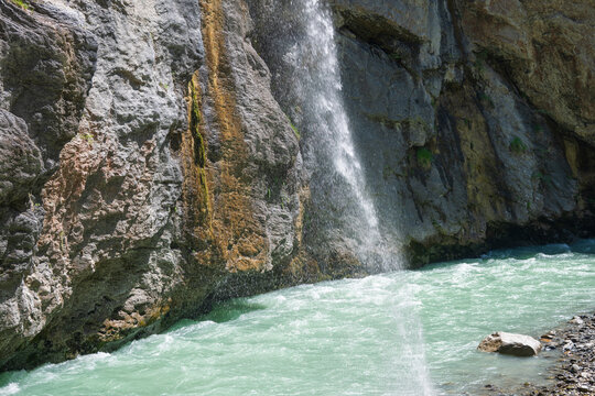 Fresh alpine water cascades down a rugged rock wall into the turquoise Aare River in Aareschlucht Gorge, Switzerland.