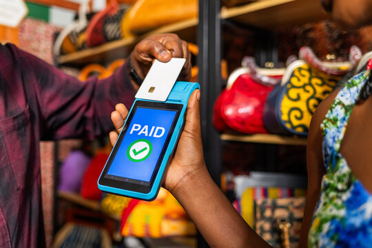 African businesswoman accepting card payment using POS terminal in her handbag shop