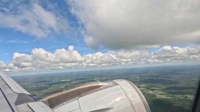A wide view of the earth seen through an airplane window, showing a beautiful landscape beneath thick clouds during daytime flight.