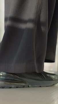 Close up of person wearing black shoes and dark pants. Footwear details include shoe texture and fabric material. Background is blurred to emphasize lower body movement indoors