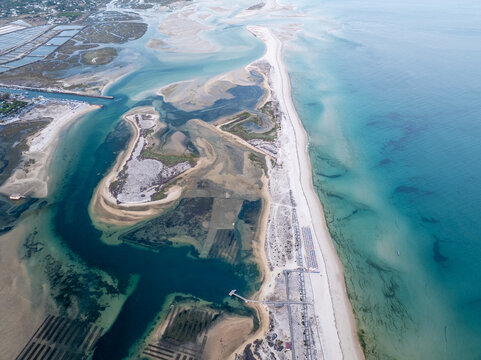 Aerial view of the Ria Formosa barrier islands and sandbanks with turquoise waters, tidal channels, and sandy beaches in the Faro District, Portugal.