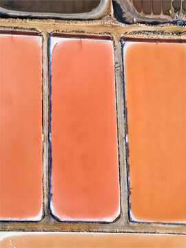 Aerial view of vibrant salt pans with distinct orange and pink water pools separated by narrow dirt paths in Faro District, Portugal.