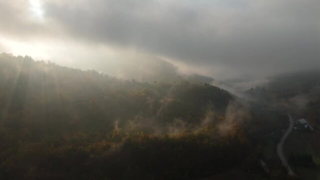 Aerial view of mountain forests shrouded in morning mist with dramatic sunbeams breaking through the clouds	