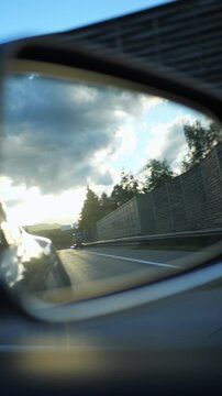 Car side mirror reflecting highway and truck during a summer evening drive