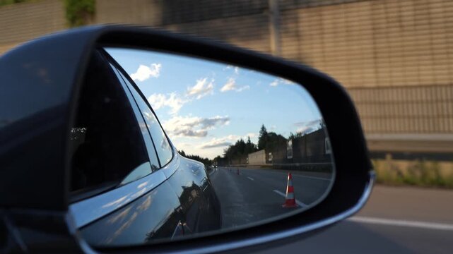 Side mirror reflecting traffic cones on a highway at golden hour