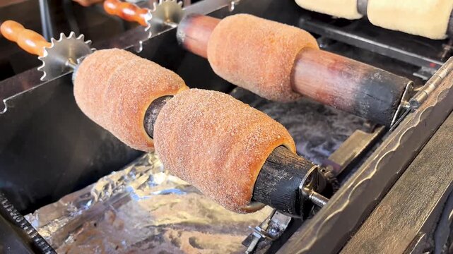 Watch as skilled bakers prepare mouth-watering trdelnik over glowing coals. This delightful pastry, rolled in cinnamon sugar, is a cherished treat from Central Europe, enjoyed in lively markets.