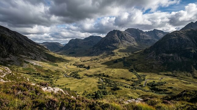 Dramatic scenic view of a vast green mountain valley with a winding stream and dark clouds in the wild highlands