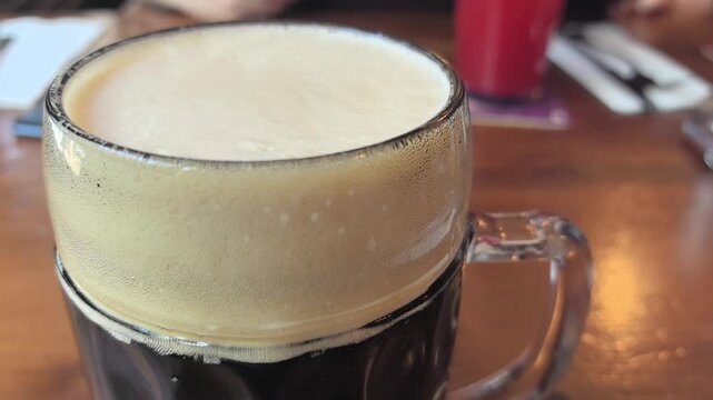 Foamy dark beer fills a glass, showcasing its rich color and creamy head. Friends enjoy drinks at a lively pub, capturing the warm atmosphere of good company and relaxation.