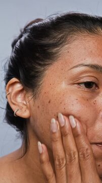 Vertical shot of young Hispanic woman applying cosmetic serum with dropper on her freckled cheek and massaging it. Perfect for skincare brand commercials or beauty routine tutorials